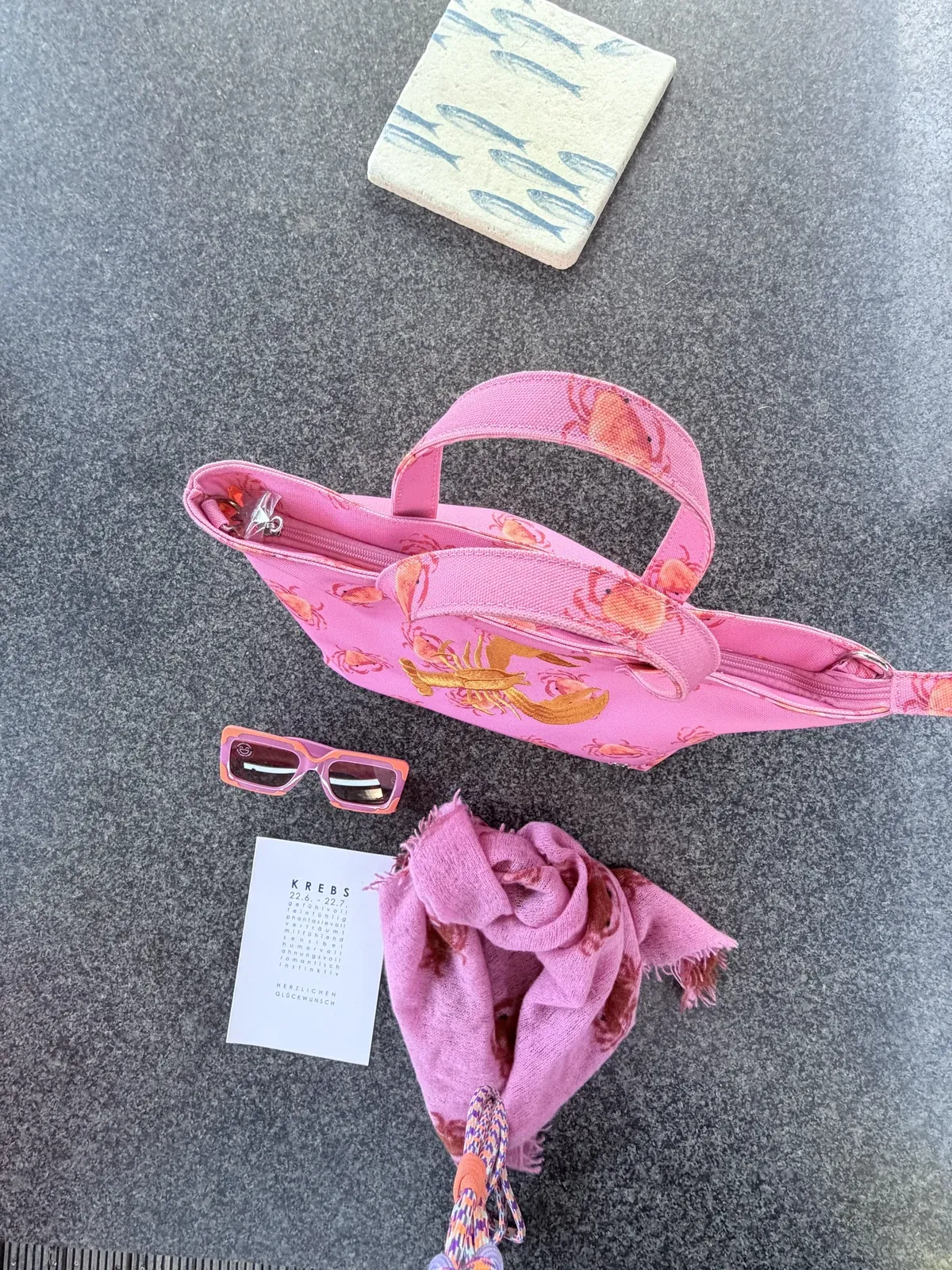 Pinke Tasche mit Krebsmotiv, pinke Sonnenbrille, Tuch und eine Sternzeichenkarte