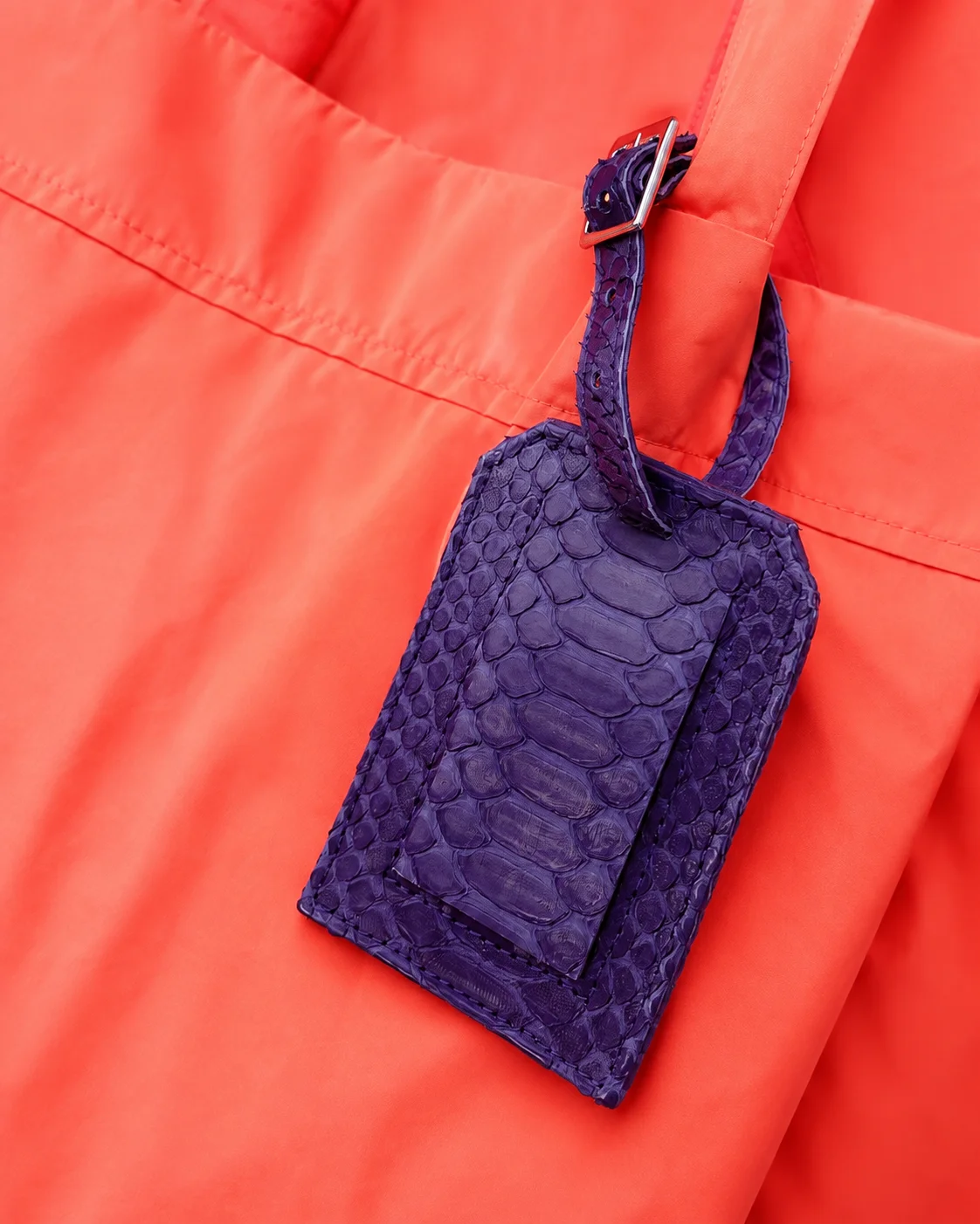 Purple snakeskin luggage tag on a coral bag as a motif for the python look