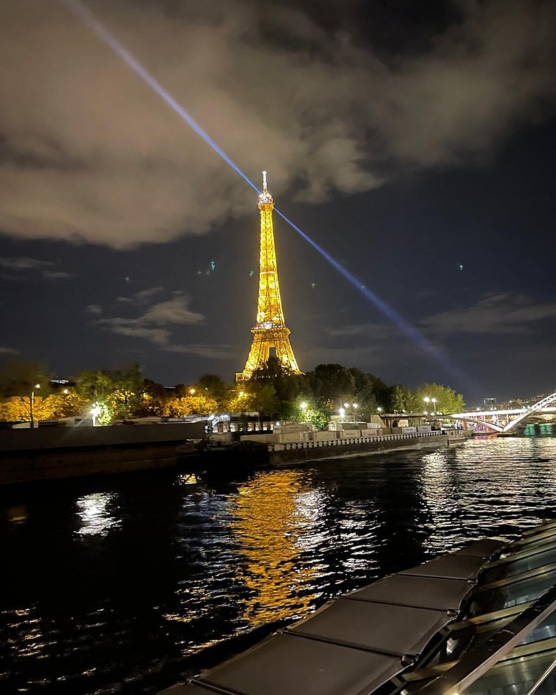 The illuminated Eiffel Tower at night above the Seine, seen from the water