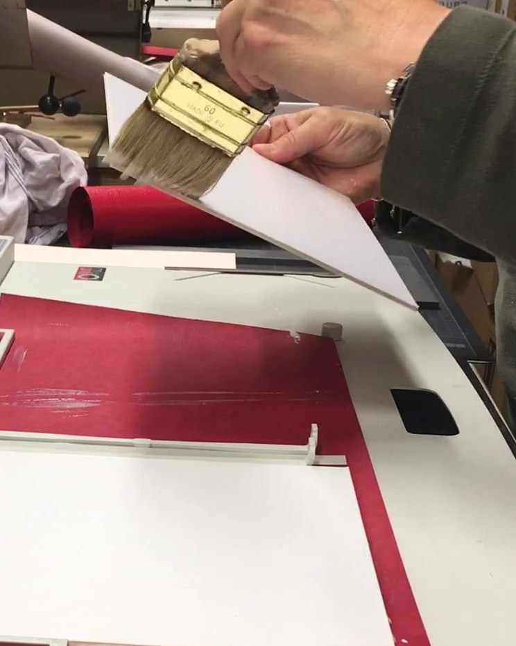 Eine Hand trägt mit dem Pinsel Leim auf einen Bogen auf