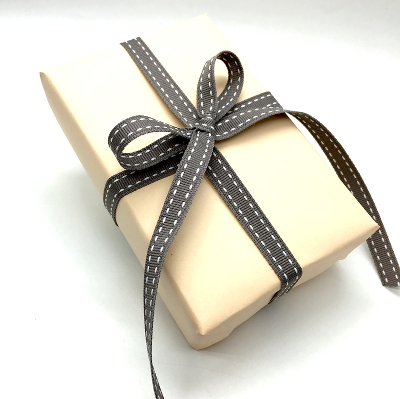 Geschenk in cremefarbenem Papier mit schmalem grauem Ripsband mit weißer Steppnaht