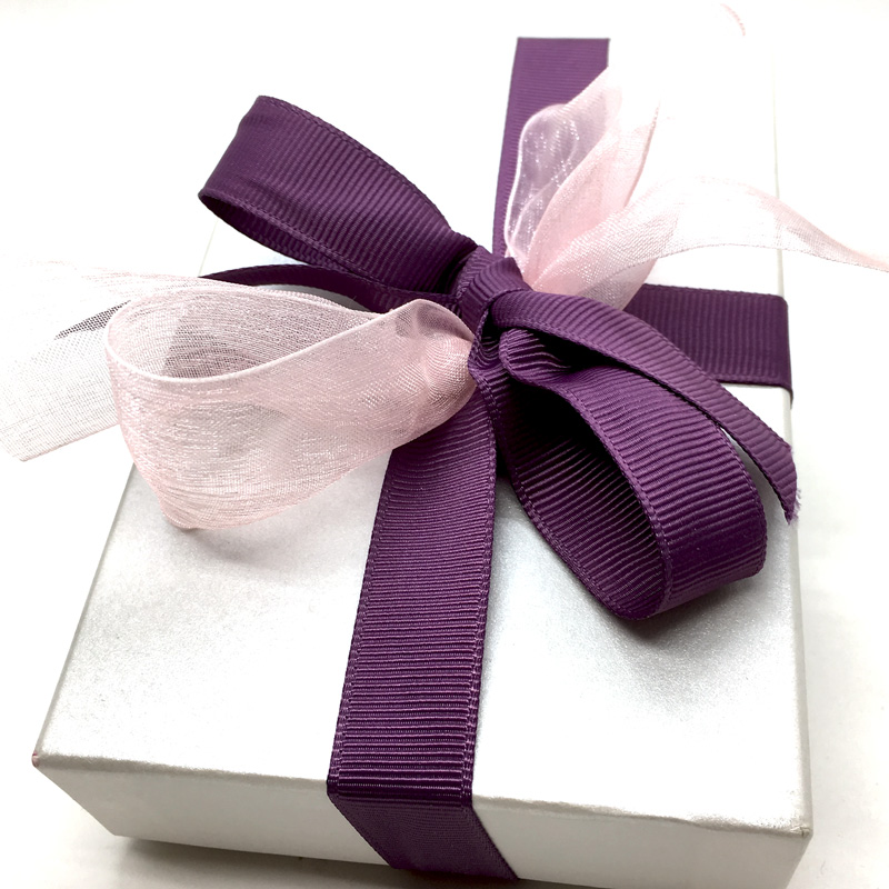 Weiße Geschenkschachtel mit Ripsband in Aubergine und einer Schleife aus rosa Organza