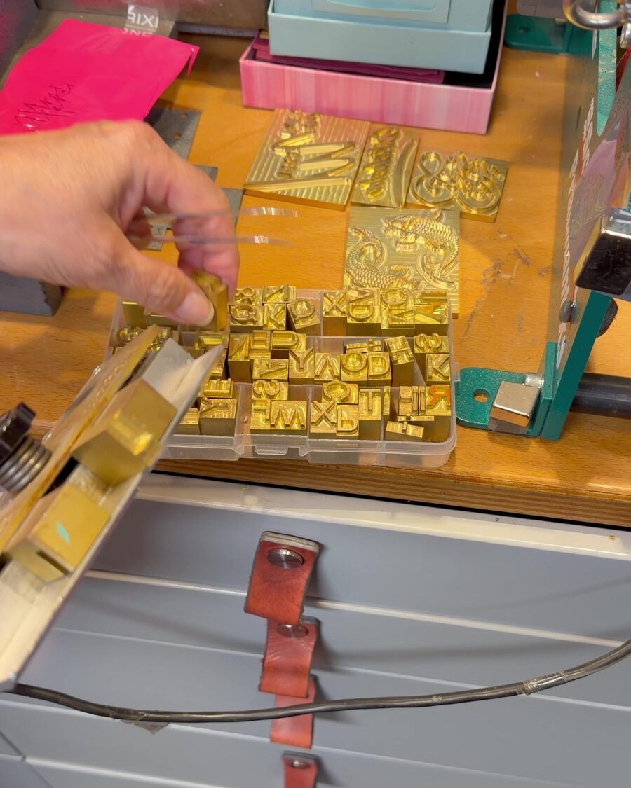 Hand nimmt Prägebuchstaben aus Messing aus dem Setzkasten