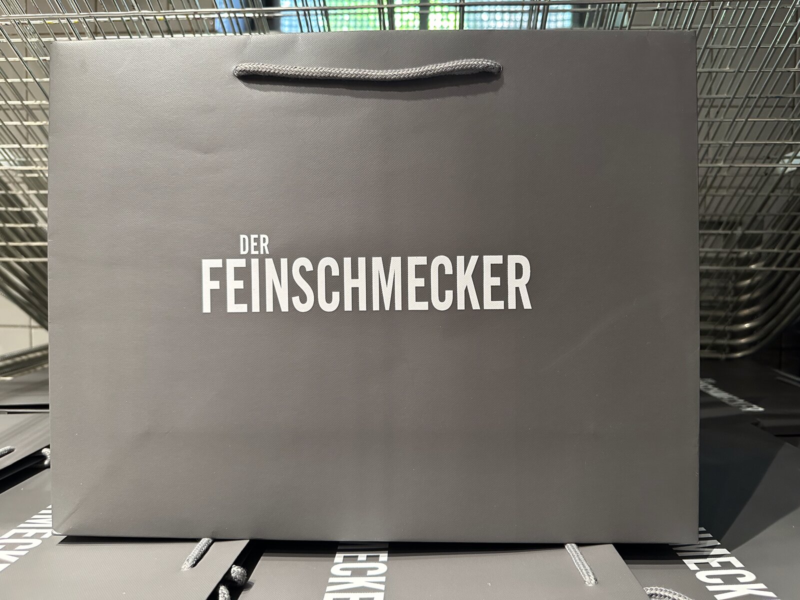 Fertige graue Tragetasche mit weißem Schriftzug Der Feinschmecker und Kordelgriff