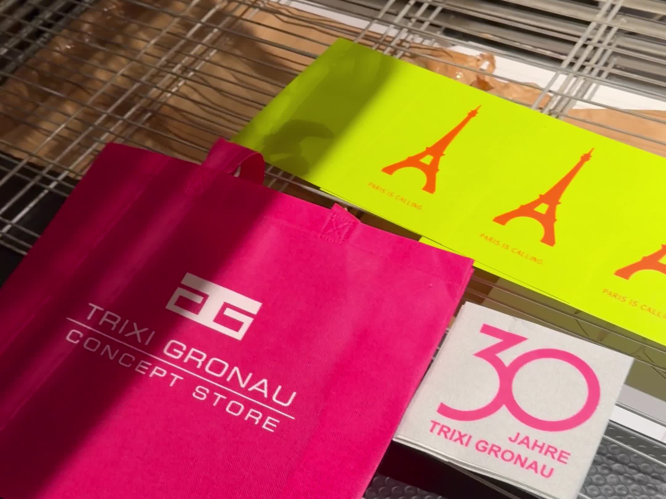 Pinke Stofftasche mit TRIXI GRONAU Logo, neongelbe Karten mit orangenem Eiffelturm und eine Serviette 30 JAHRE TRIXI GRONAU