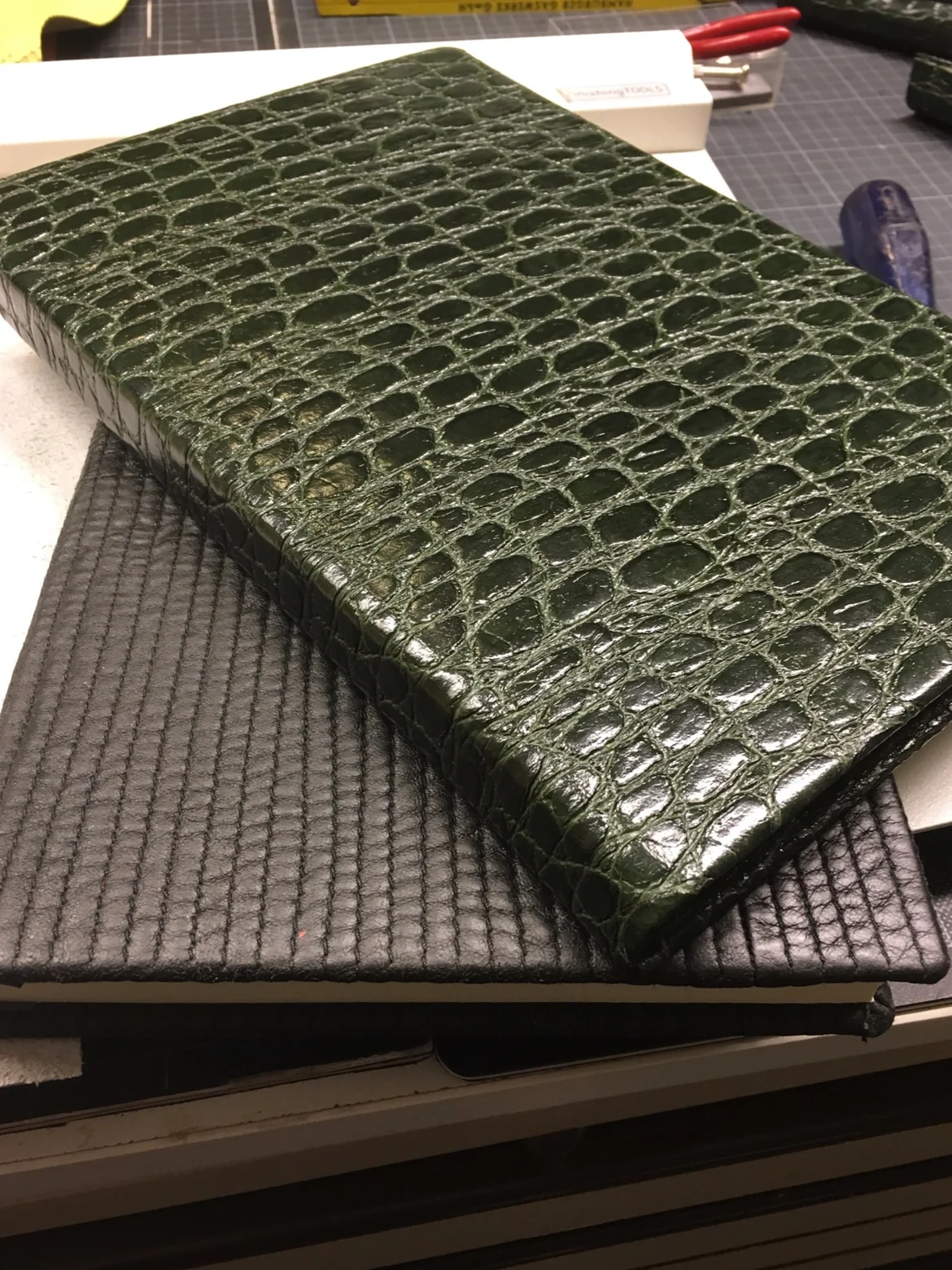 Fertiger Bucheinband mit dunkelgrüner Croco-Prägung liegt auf einem schwarz bezogenen Buch, die Kanten sind sauber gearbeitet