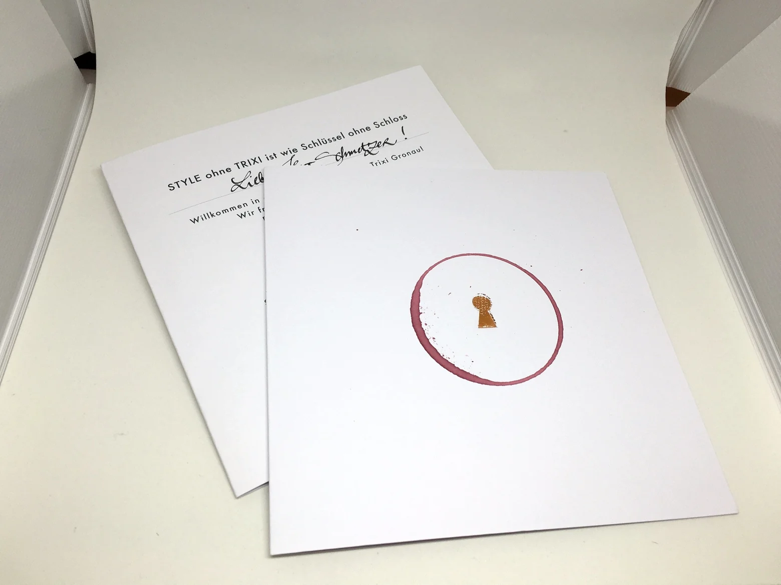 Gedruckte Einladung mit geprägtem Schlüsselloch in Gold und einem Kreis, der mit dem Rand eines Rotweinglases auf das Papier gesetzt wurde