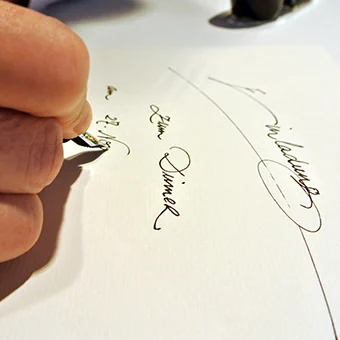 Kalligraphie im Atelier TRIXI GRONAU: eine Hand schreibt mit der Feder einen Namen in Schreibschrift auf Papier