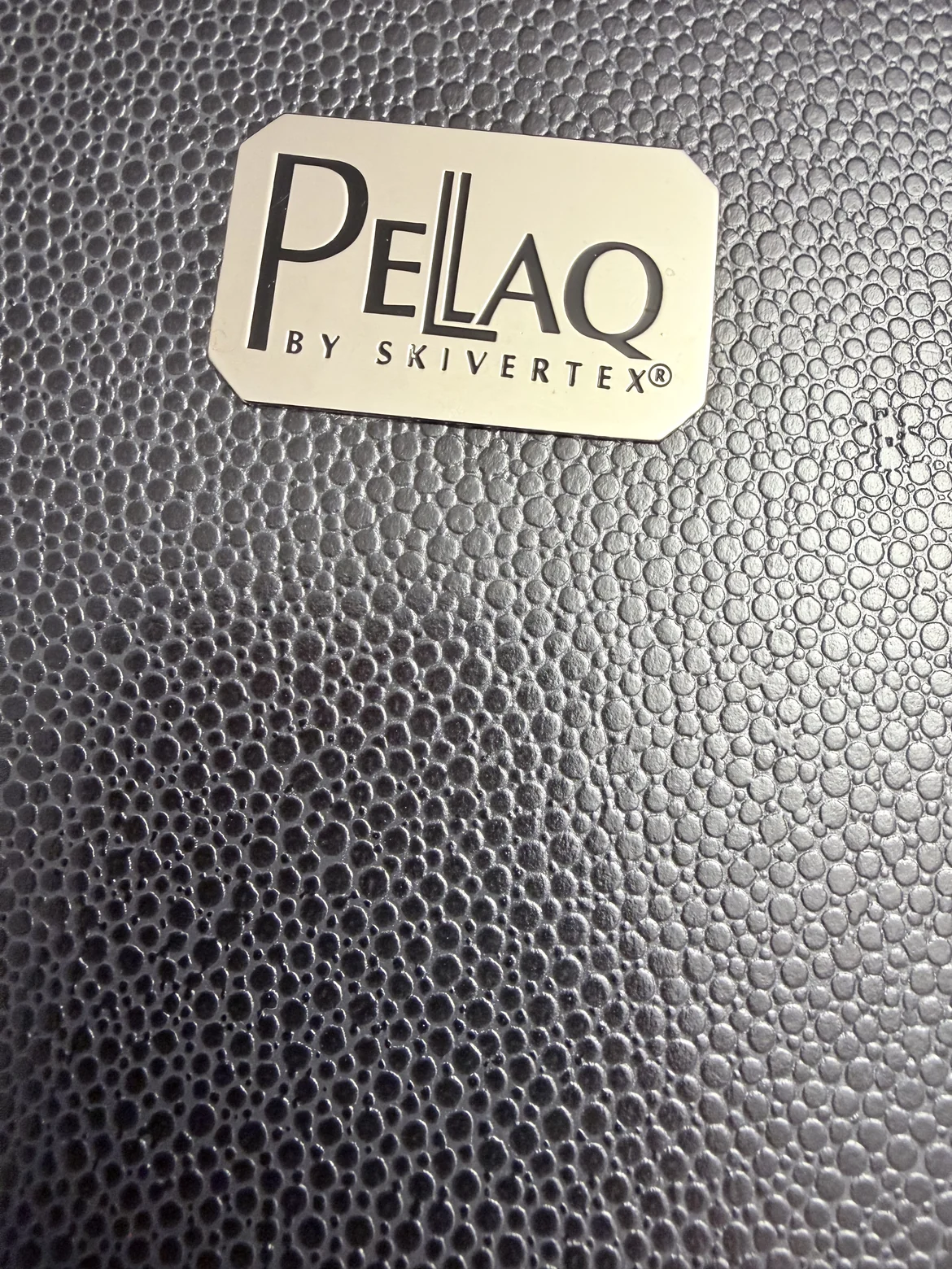 Dark material surface with a fine pearled embossing, with the label Pellaq by Skivertex resting on it