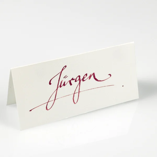 Handgeschriebene Tischkarte aus dem Kalligraphie-Studio von TRIXI GRONAU, weinroter Name auf cremefarbenem Karton